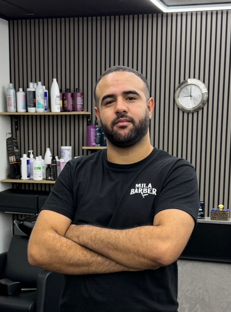 Hassan, de pie con los brazos cruzados junto al sillón de la barbería